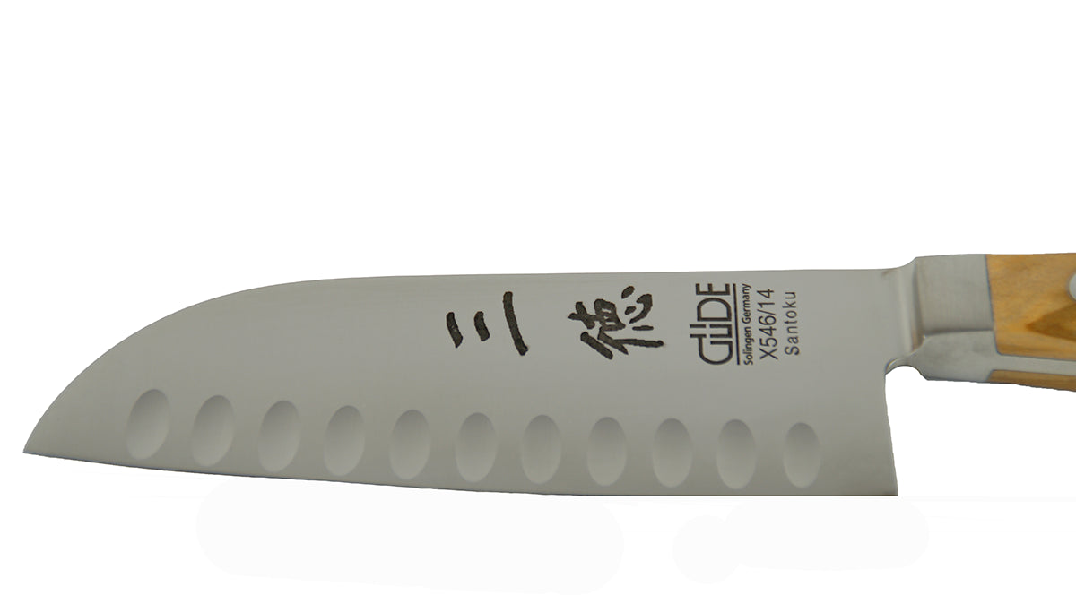 GÜDE Klinge des Santoku Alpha Olive X546/14 – Japanisches Kochmesser mit Kullenschliff 14 cm Klingenlänge mit Olivenholz-Griff auf weißem Hintergrund