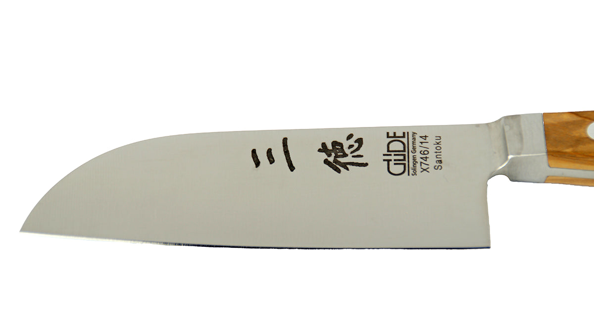 GÜDEKlinge des Santoku Alpha Olive X746/14 – Japanisches Kochmesser mit glatter 14 cm langen Klinge und Olivenholz-Griff auf weißem Hintergrund