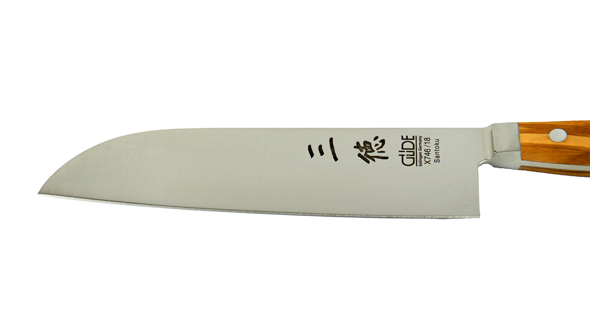 GÜDE Klinge des Santoku Alpha Olive X746/18 – Japanisches Kochmesser mit glatter 18 cm langen Klinge und Olivenholz-Griff auf weißem Hintergrund